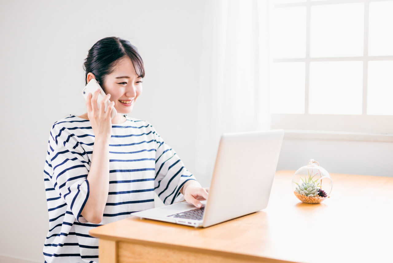 スマホで電話しながらパソコンをさわる女性